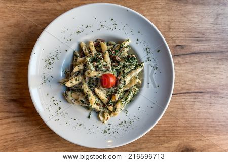 Colorful plate with penne pasta with prosciutto and spinach on a table