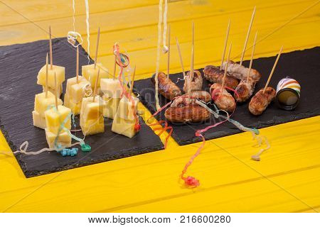 Sausages on sticks and cheese and pineapple nibbles. Leftover fun party food with party popper streamers on bright yellow table.