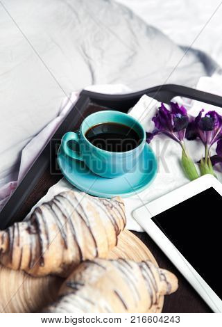 Delicious breakfast in bed with flowers. Croissant with coffee and a tablet for rest