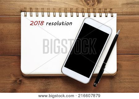 2018 resolution on blank notebook paper and smart phone on wood background new yaer business and technology concept mock up