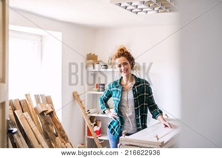 Small business of a young woman. Beautiful young woman worker in workroom. Female carpenter standing by her products.