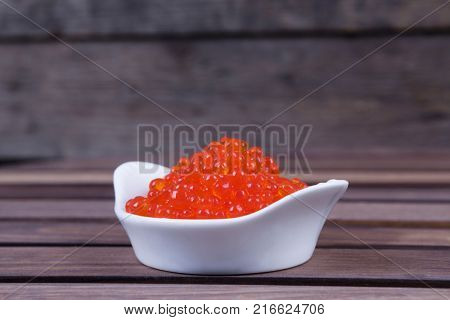 red salmon caviar in white bowls on wooden background