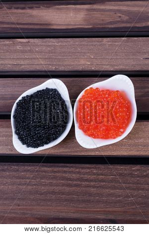 black sturgeon hausen caviar with red salmon caviar in white bowls on wooden background