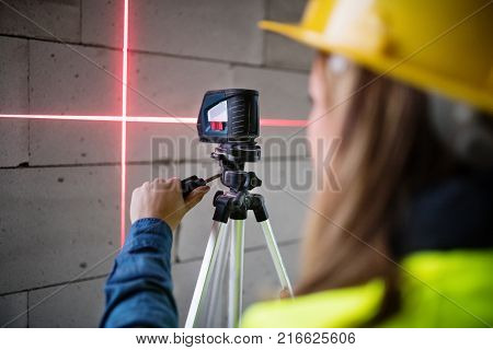 Female worker on the building site. Beautiful young woman with line laser level. House construction.