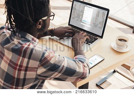 african american man using laptop with linkedin website and smartphone with shazam appliance