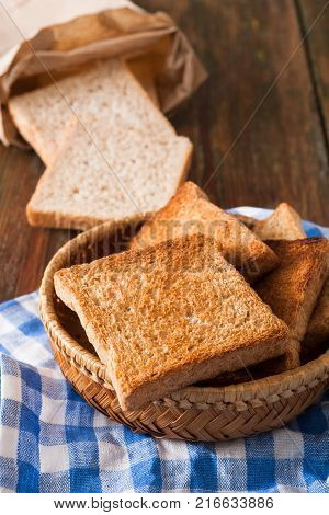 Breakfast background, white bread toasts in wicker breadbasket on checkered table napkin half covering wooden table, closeup, vertical