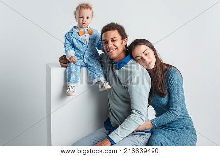 A happy family of afro man and caucasian woman and child on white studio background