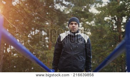 Young handsome athlete man doing push-ups exercise on bars in winter park outdoors