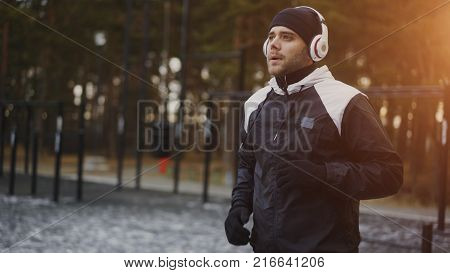 Attractive man in headphones doing warm-up exercise preparing for jogging while listening music in winter park outdoors