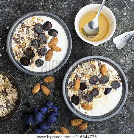 Breakfast from healthy seasonal ingredients: granola, flakes, honey, dark grapes, almonds in a serving gray pial on a gray grunge background. Top view. Vegetarian Organic Food Concept