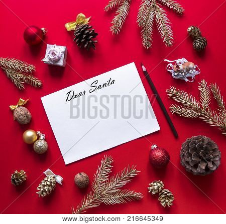 on a red raspberry background, New Year and Christmas decorations and spruce gold branches are arranged in a circle, and in the center lies a white sheet with a letter to Santa Claus and a pencil