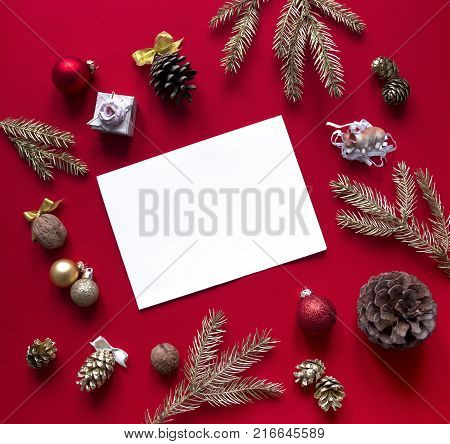 on a red raspberry background, New Year and Christmas decorations and spruce gold branches are arranged in a circle, and in the center lies a white sheet and a pencil