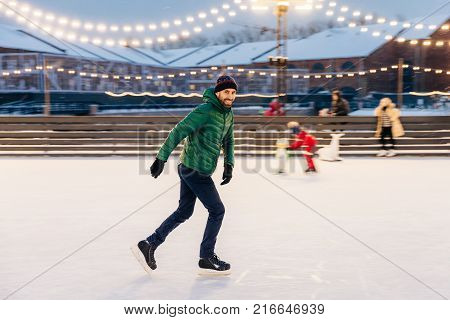 Outdoor Shot Of Unexperienced Male Skater Uses Skate Aid For Go Skating On Ice, Being In Good Mood,
