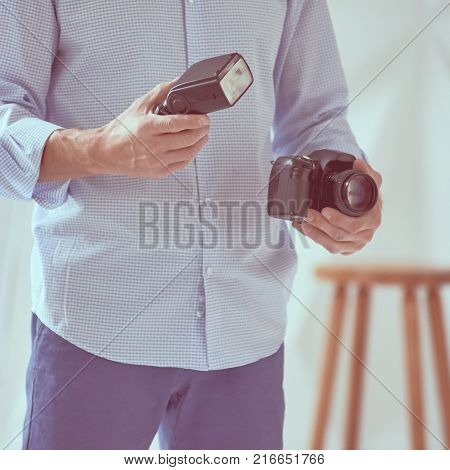 Closeup of young man holding digital camera with synchronizer and flash in studio, focus is on hand with flash, image with vintage toning