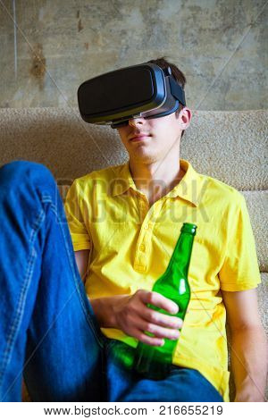 Young Man in VR Glasses hold Bottle of a Beer on the Sofa