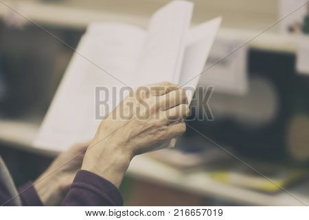 Close-up of hands of the elderly person with open book, bookstore, library. Real scene. Education concept, Self-study, reading fiction, pension, interests in the elderly, life style. Toned background