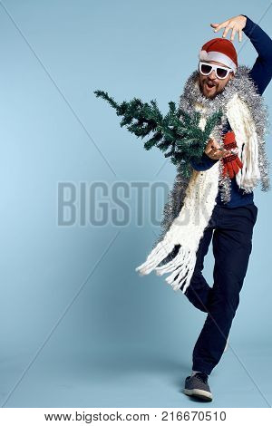 man with an artificial Christmas tree posing in full growth on a light blue background, free space for copying, new year.