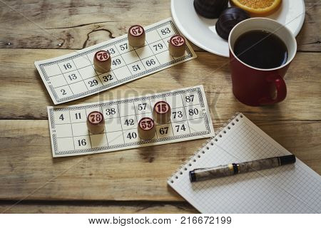 Cards And Chips For Playing Bingo On A Wooden Table. Cup With Coffee