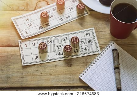 On A Wooden Bingo Table Game, A Cup With A Coffee, A Biscuit And An Orange Slice