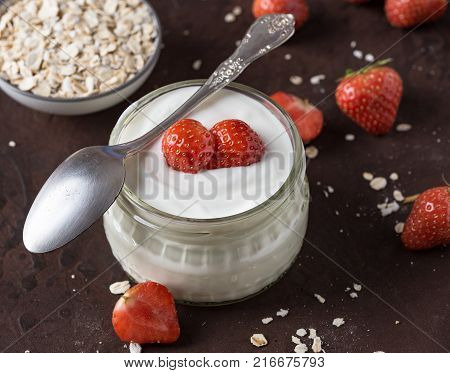White yogurt in glass bowl with spoon and starwberries on rustic background.