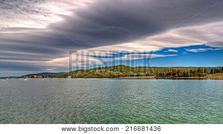A spectacular inspirational brightly coloured cloudy sea water panoramic seascape landscape featuring white cirrus cloud formation in a vivid blue sky with ocean water reflections. Gosford Australia.