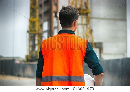 Construction engineer or worker or construction foreman holding safety white helmet and Blueprint standing in construction site.