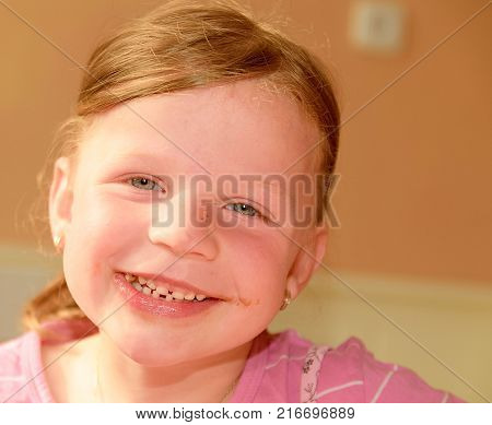 Kid girl eats chocolate cream spread on bread. Chocolate sweet food snack. Happy girl has a snack in the kitchen. A cute small girl smiles. A small girl with chocolate cream stains on face