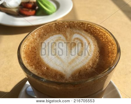 Latte coffee servied in a glass at a cafe with delicious food in the background.