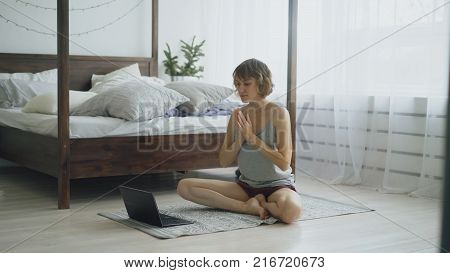 Young attractive woman doing yoga exercise and watching tutorial lesson on laptop computer in bedroom at home in the morning