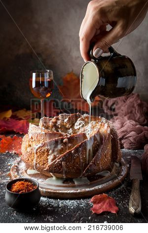 Bundt cake with saffron and rum covered with white glaze on rustic background with autumn decorations