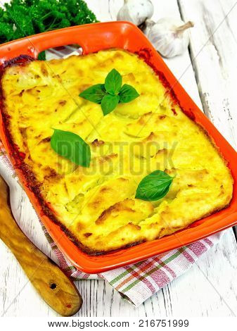 Casserole from mashed potatoes with fish fillets in a brazier on a towel on a wooden plank background