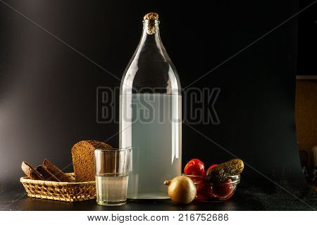 Ukrainian national drink and snack. The big bottle and glass of moonshine isolated on black background. Russian vodka and snack.