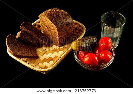 Salted cucumber with tomatoes in glass vase and loaf of fresh rye bread with slices isolated on black background.