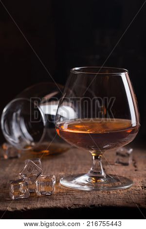 Glass of brandy or cognac on old oak wooden table. Dark photo.