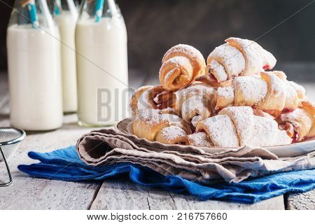 Rugelach with jam filling on plate with milk on wooden background