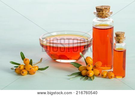 Sea buckthorn and two bottles bowl with sea buckthorn oil on blue table