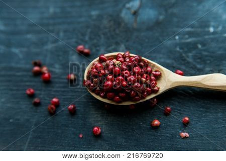 Close up wooden spoon with pink peppercorn on dark background