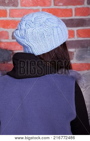 girl in hat and fur coat, against a brick wall background