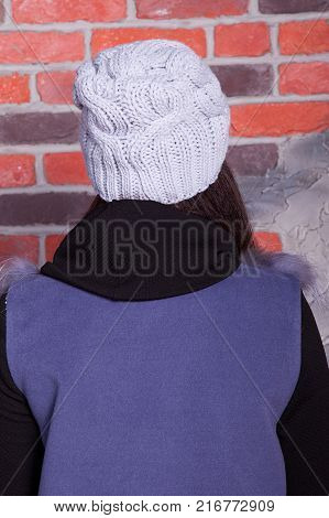 girl in hat and fur coat, against a brick wall background