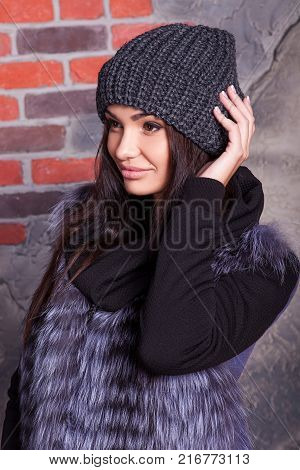 girl in hat and fur coat, against a brick wall background