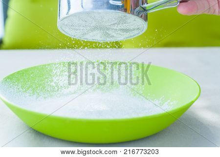 Close up male hand sifting powdered sugar in green plastic bowl