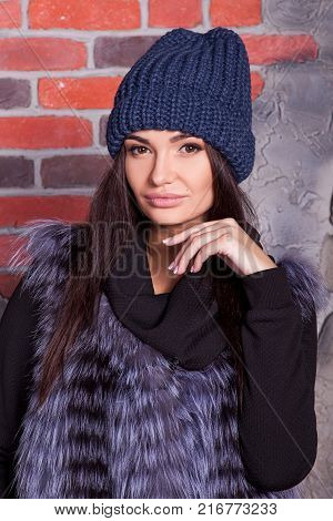 girl in hat and fur coat, against a brick wall background