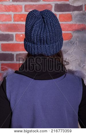 girl in hat and fur coat, against a brick wall background