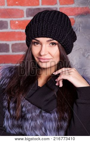 girl in hat and fur coat, against a brick wall background
