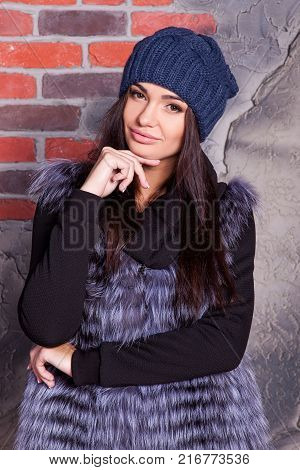 girl in hat and fur coat, against a brick wall background