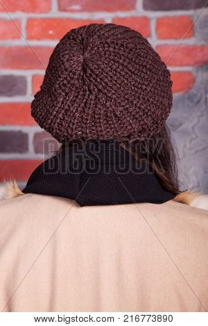 girl in hat and fur coat, against a brick wall background