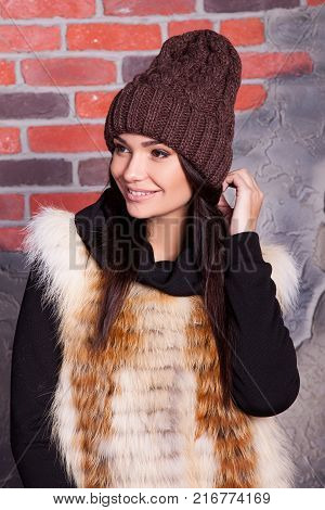 girl in hat and fur coat, against a brick wall background