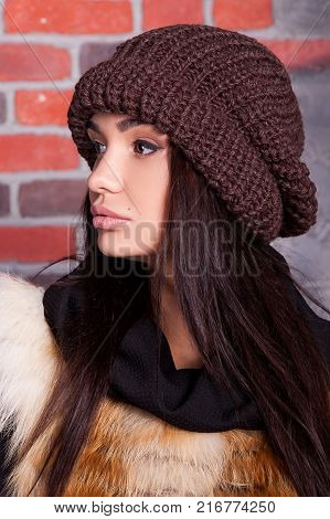 girl in hat and fur coat, against a brick wall background