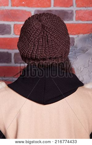 girl in hat and fur coat, against a brick wall background