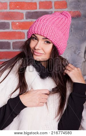 girl in hat and fur coat, against a brick wall background